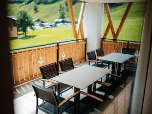 A terrace with tables and chairs, a wooden fence, and a view of a green landscape with houses.