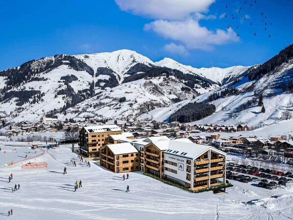 A snow-covered ski resort with wooden buildings, including a hotel named "Carpe Solem," and a ski slope with skiers.