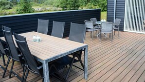 An outdoor deck with a table and chairs, surrounded by a wooden deck and a black wall. - Holiday Home in Brovst (Brovst)