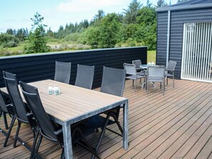 An outdoor deck with a table and chairs, surrounded by a wooden deck and a black wall. - Holiday Home in Brovst (Brovst)