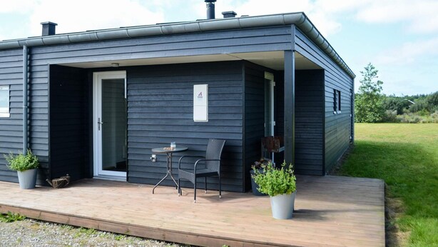 A modern, dark-colored house with a covered porch, a small table, and two chairs. - Holiday Home in Brovst (Brovst)