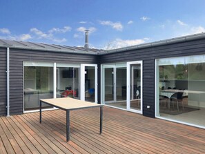 A modern house with a wooden deck, large sliding glass doors, and a chimney. - Holiday Home in Brovst (Brovst)