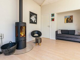 Una sala moderna con una estufa de leña, un sofá gris y un taburete pequeño.