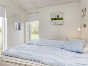 A bedroom with a bed, a window, a door, and a wall-mounted artwork.