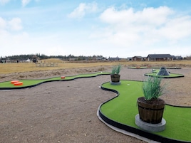 Un campo de mini golf con zona de juego arenosa, superficies de césped para los putts y jardineras de madera.