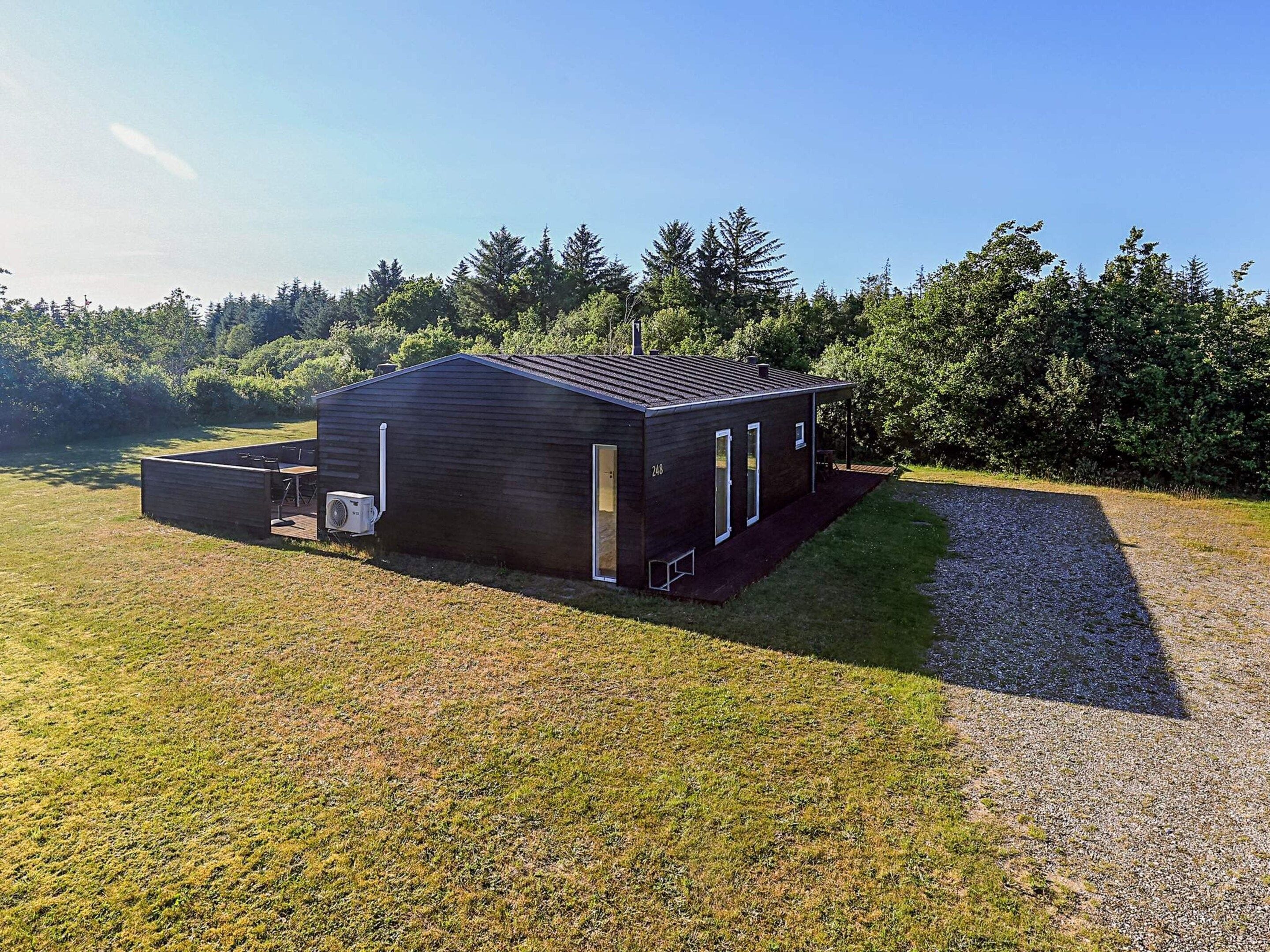 A modern, single-story building with a dark exterior, a covered outdoor seating area, and a gravel driveway.