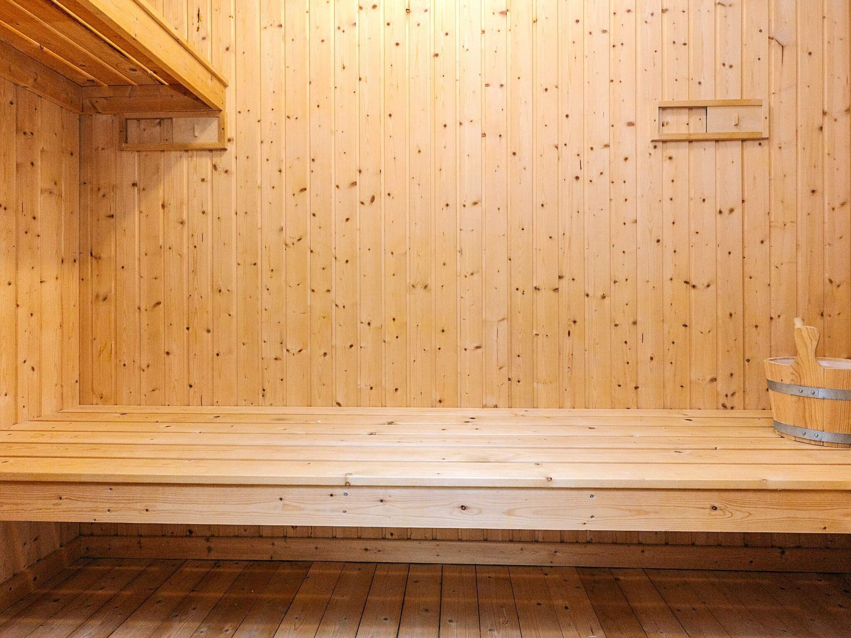 A wooden sauna room with a sloped ceiling, a wooden bench, and a metal bucket.