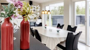 Un coin repas avec une table et des chaises, un vase rempli de fleurs posé sur la table et une fenêtre laissant entrer la lumière du jour.