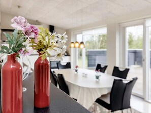 A dining area with a table and chairs, a vase with flowers on the table, and a window with daylight.