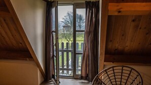 A room with a sloped ceiling, a window with curtains, and a wicker chair. - Superb Holiday Home on a Mini Campsite Near the Beach (Vrouwenpolder)