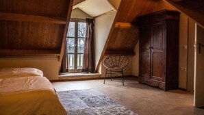 A bedroom with a sloped ceiling, a large window, a bed, a chair, and a wardrobe. - Superb Holiday Home on a Mini Campsite Near the Beach (Vrouwenpolder)