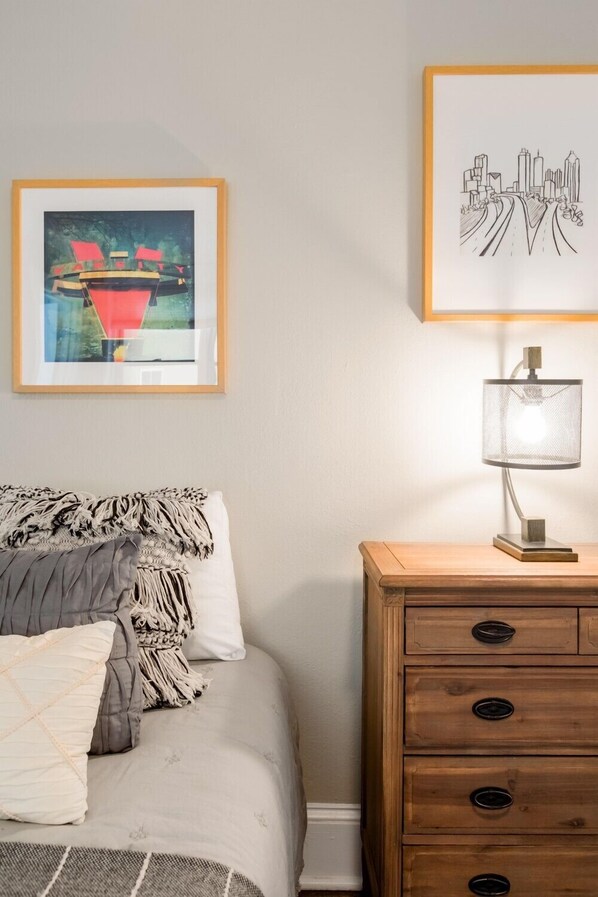 A bedroom with a bed, a nightstand with drawers, and two framed artworks on the wall.