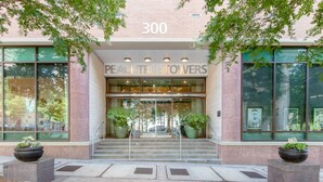 La entrada a Peachtree Towers, con fachada de vidrio, exterior de ladrillo y plantas en macetas en los escalones.