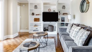 Una sala de estar con un sofá gris, una mesita de centro y un televisor sobre un mueble blanco.