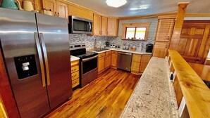 A kitchen with wooden cabinets, stainless steel appliances, a granite countertop, and a window with blinds. - Sunset View over the Mountains! Rustic Cabin w/ Hot Tub (Almond)