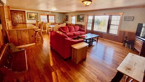 A spacious living room with a red sofa, wooden coffee table, and a dining area with wooden chairs and a table. - Sunset View over the Mountains! Rustic Cabin w/ Hot Tub (Almond)