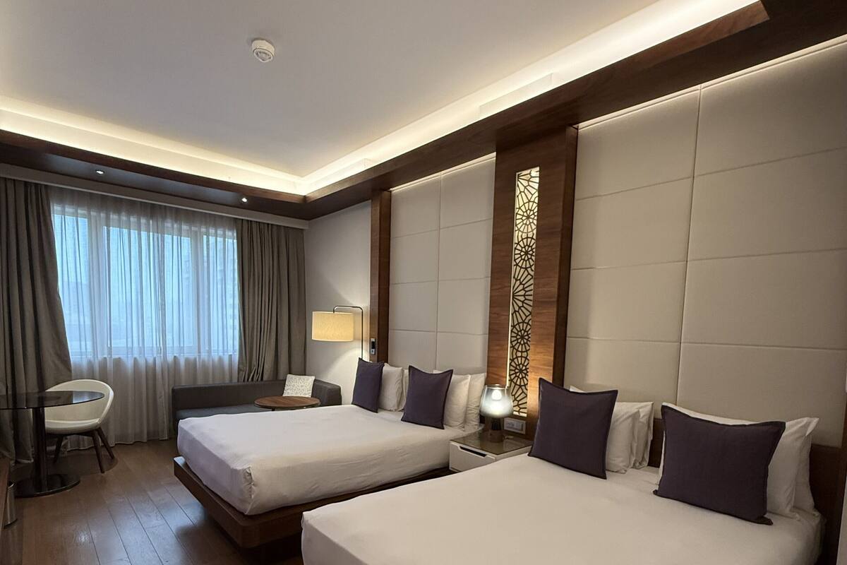 Habitación de hotel con dos camas, un escritorio, una silla y una ventana con cortinas.
