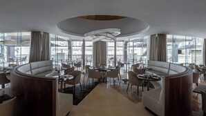 Un moderno vestíbulo de hotel con una zona de estar curvilínea, una mesa redonda central y grandes ventanales que ofrecen vistas de la ciudad.