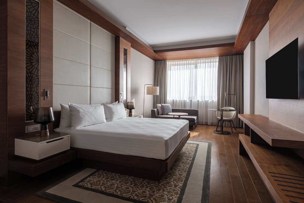Habitación de hotel moderna con una cama grande, un escritorio, una silla, un televisor y una ventana con cortinas.