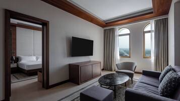 Habitación de hotel moderna con una cama grande, televisor de pantalla plana, sofá, mesa de centro y vistas a la ciudad a través de amplios ventanales.