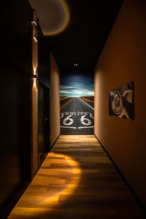 A hallway with a wooden floor leading to a road painted on the wall, a framed picture on the wall, and a door on the left.