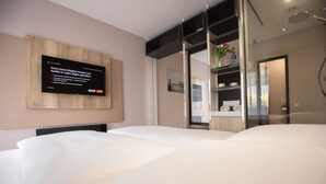 Una habitación de hotel con una cama grande, un televisor montado en la pared y una cabina de ducha de vidrio.