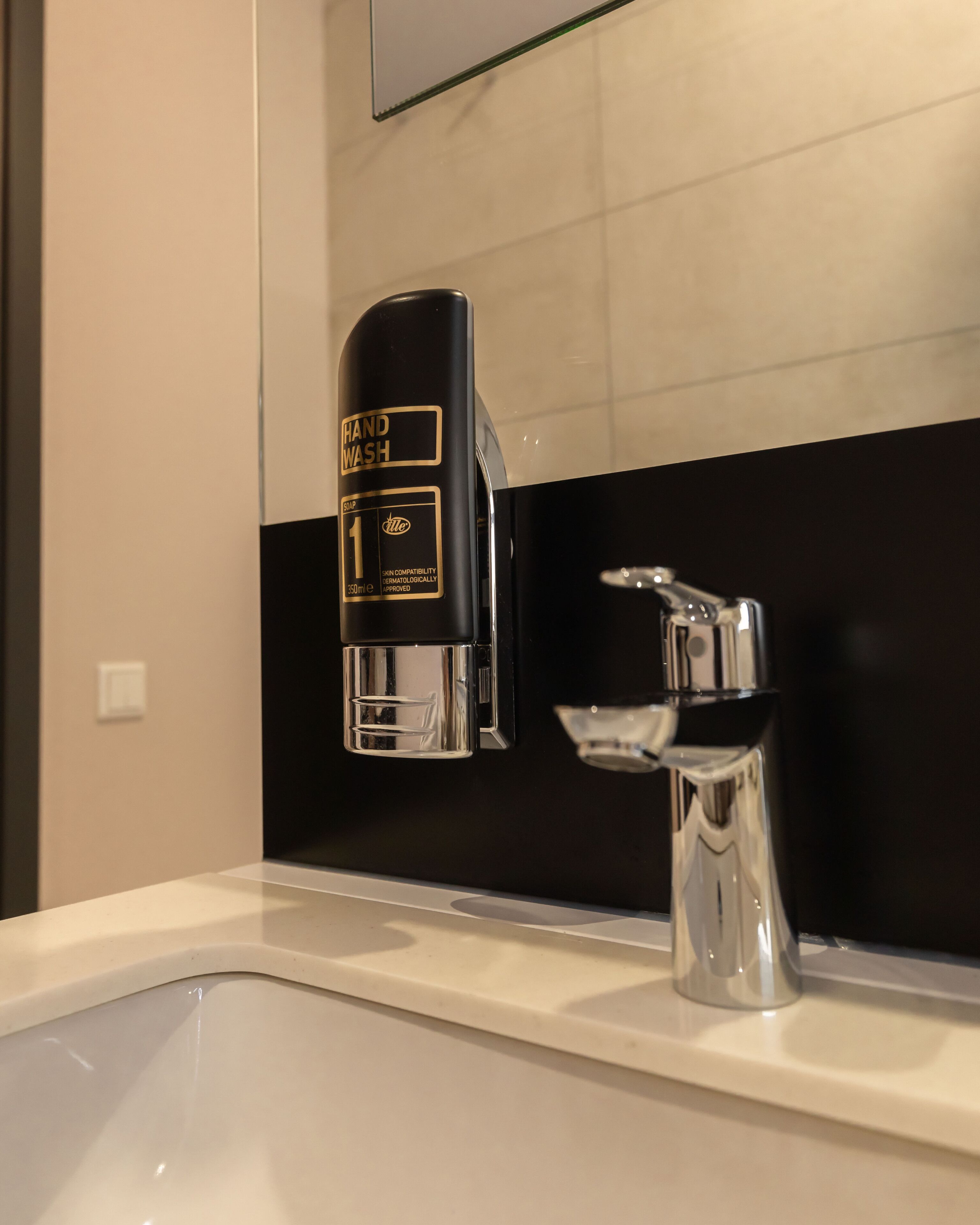 Un baño moderno con un lavamanos blanco y negro, un grifo cromado y un dispensador de jabón.