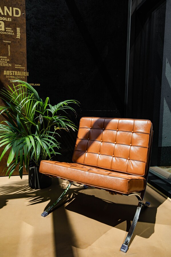 A brown leather chair with a cushioned backrest and metal legs, positioned next to a potted plant.