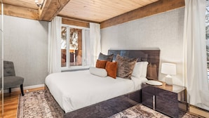 A bedroom with a large bed, a nightstand, a chair, and a window with curtains. - Quiet & Convenient With Great Amenities. Close To Downtown. Large Pool, HT, Fitness Rm. Parking (Aspen)