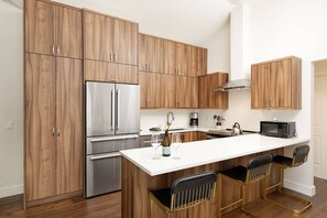Una cocina moderna con armarios de madera, un refrigerador de acero inoxidable, un microondas y una encimera blanca.