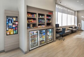 Un hall d’hôtel comprenant un espace salon, un kiosque de vente de boissons et de collations, et un comptoir d’accueil.