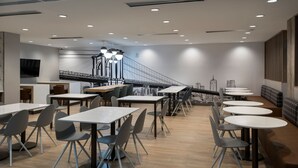 A modern restaurant with multiple tables and chairs, a staircase, and a cityscape mural on the wall.