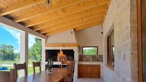 A dining area with a wooden table and chairs, a stone fireplace, and a stone wall. - Four Bedroom Holiday Home (Turjaci)