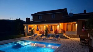 A house with a swimming pool, outdoor seating, and a well-lit patio area. - Four Bedroom Holiday Home (Turjaci)