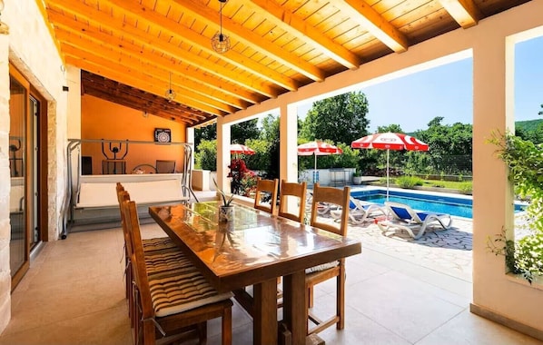 A covered outdoor dining area with a pool and umbrellas.