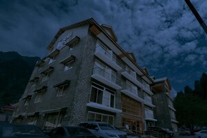 Un hotel de varios pisos con fachada de ladrillo, balcones y una zona de estacionamiento.