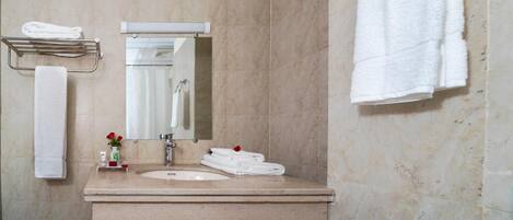 A bathroom with a sink, mirror, towel rack, and a vase with red flowers.