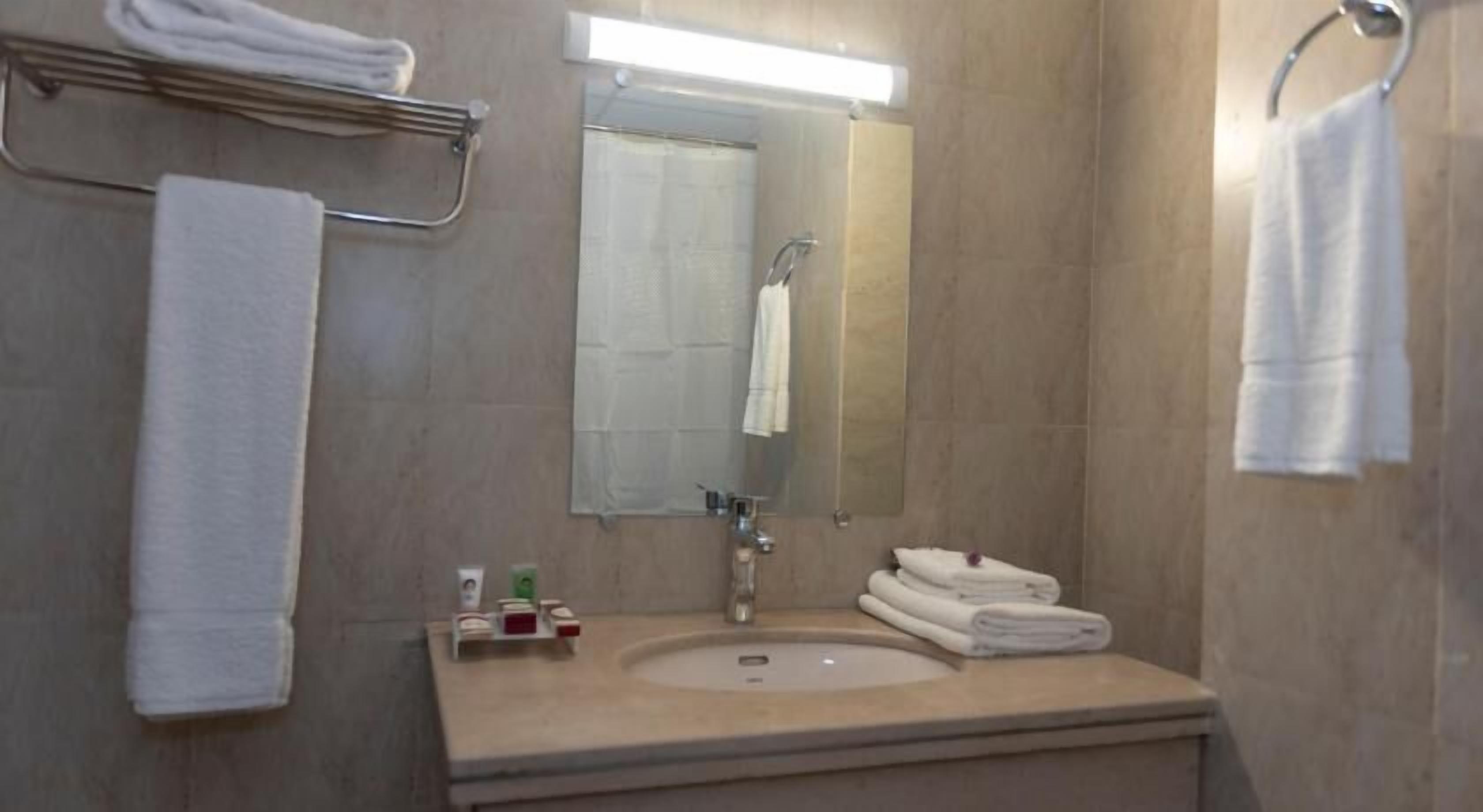 A bathroom with a sink, mirror, towel rack, and a small shelf with toiletries.