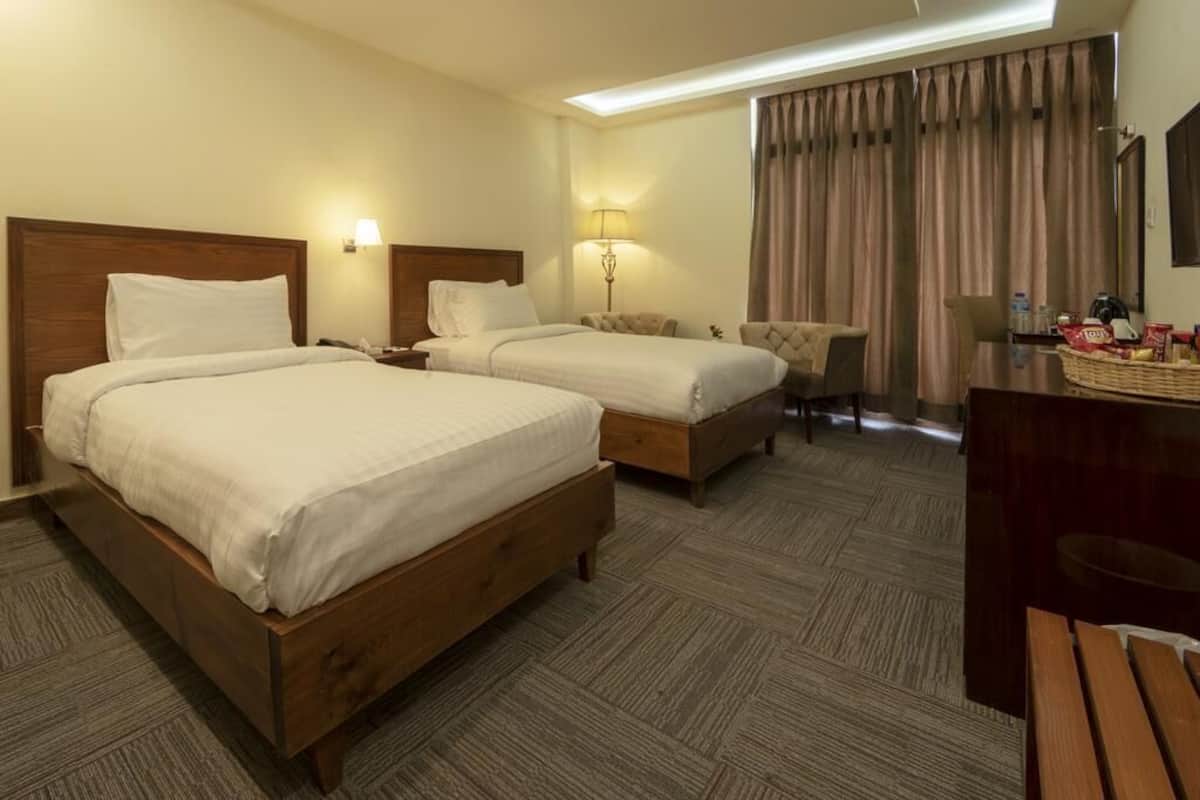 A hotel room with two wooden beds, a desk, a chair, and a dining table.