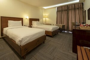 Quarto de hotel com duas camas de madeira, uma escrivaninha, uma cadeira e uma mesa de jantar.
