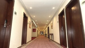 A hotel hallway with wooden doors, numbered room signs, and a patterned carpet. - Hotel One Naran (Balakot)