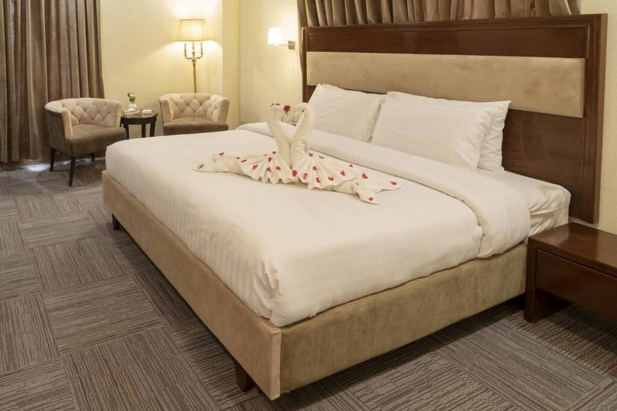 A hotel room with a large bed, two armchairs, a nightstand, and a lamp.
