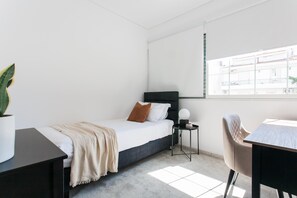 A modern bedroom with a bed, bedside table, chair, and a window with a view of buildings. - Splendid 3BR close to Olympic Stadium (Marousi)