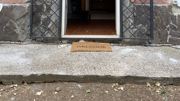 A building entrance with a metal gate, a small window above the door, and a welcome mat on the ground. - Casale Colle dei Pini (Anguillarese-colle Due Pini)