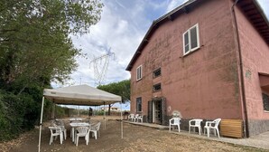 A rustic building with a red exterior, white outdoor seating, and a tent. - Casale Colle dei Pini (Anguillarese-colle Due Pini)