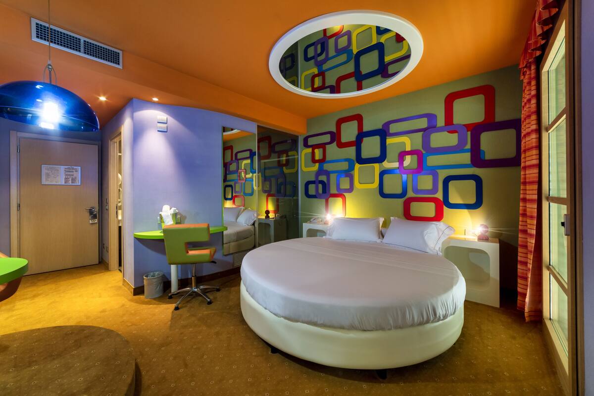 Een hotelkamer met een groot bed, een bureau, een stoel en een kleurrijk wandontwerp.