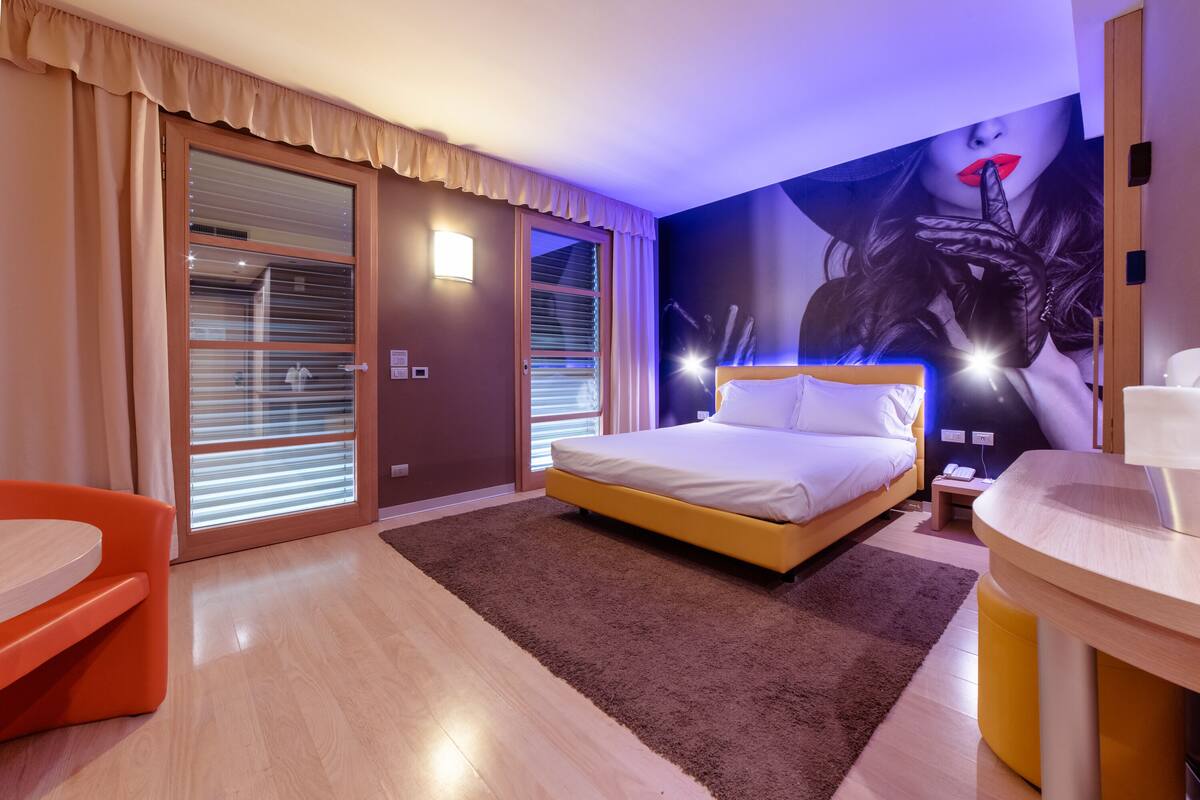 Een hotelkamer met een bed, een bureau, een stoel en een groot raam met gordijnen.