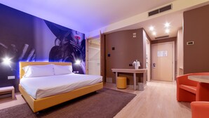 A modern hotel room with a large bed, a small desk, and a round orange table. - Motel Hotel Piranha (Casalino)