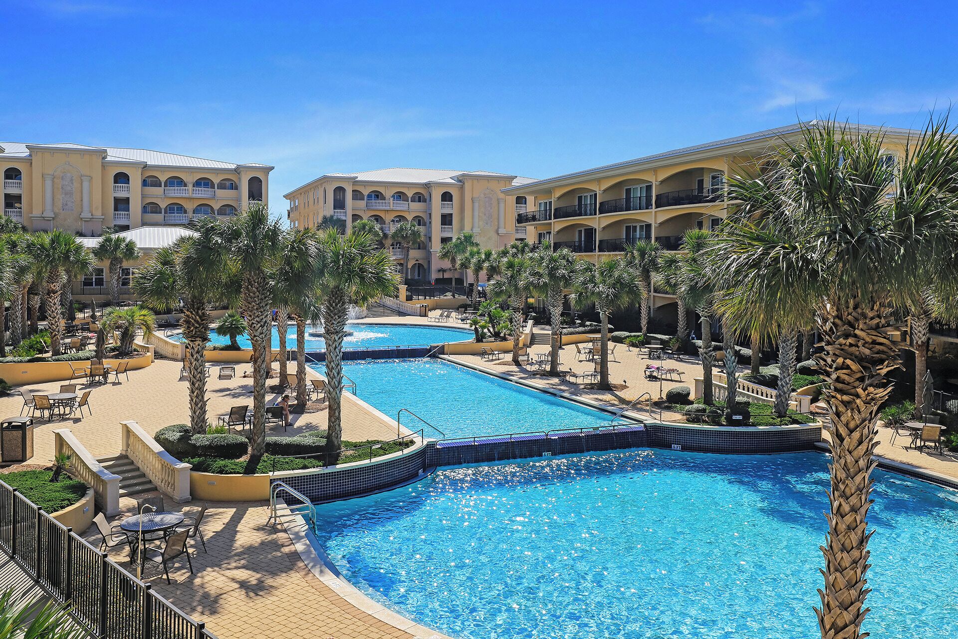 Ein Resort mit mehreren Schwimmbecken, umgeben von Palmen und Liegebereichen.