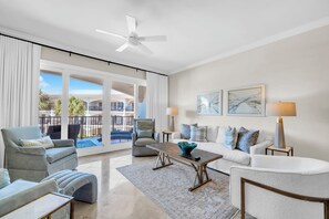 A spacious living room with a ceiling fan, large windows, and a view of a pool and building. - Adagio E-204 Poolside 3/3 Unit - Gorgeous 2nd Floor Unit! (Santa Rosa Beach)